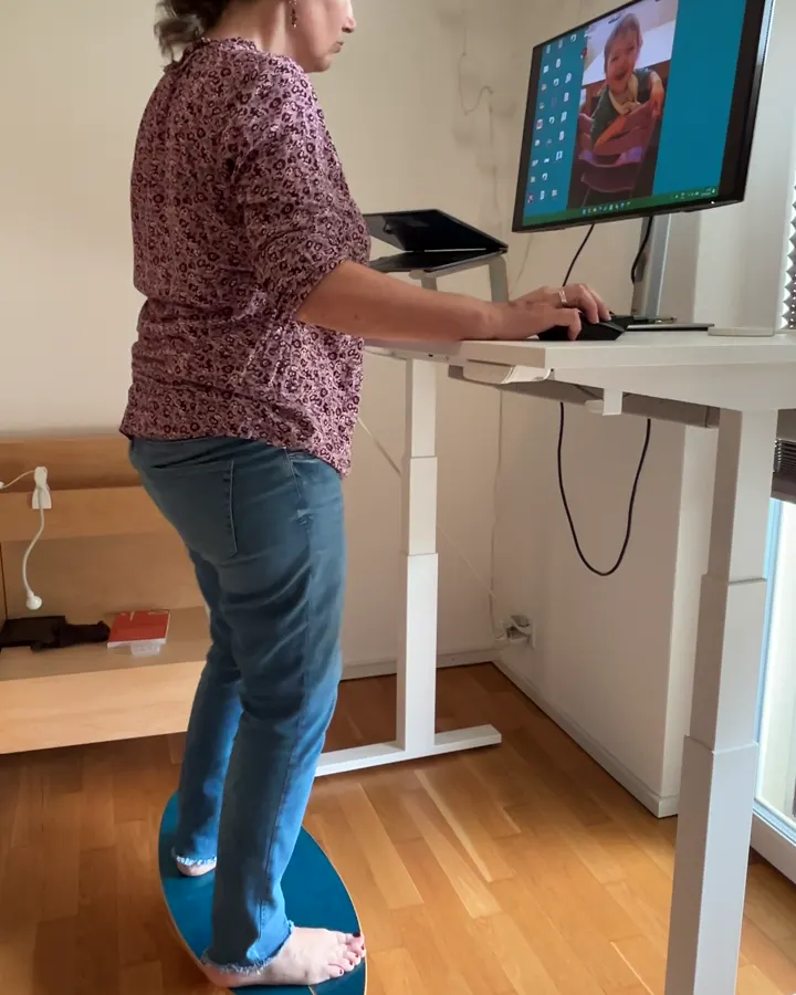 Frau arbeitet am Stehschreibtisch auf dem Balance Board